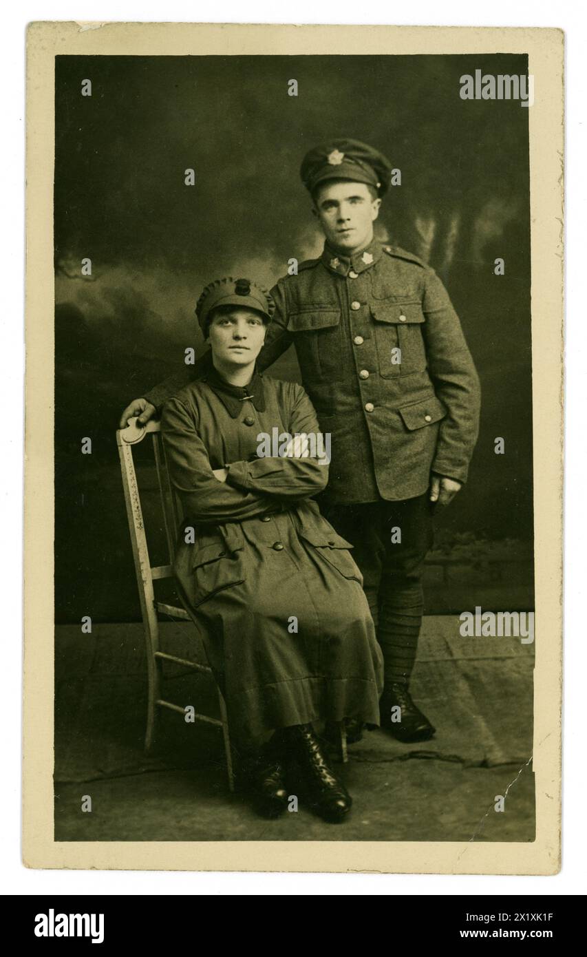 Original WW1 era postcard portrati of women's army auxiliary corps  (W.A.A.C.) recruit wearing a standard issue trench coat, cap, maybe a driver seated, with Canadian army boyfriend, who wears a cap with a maple leaf badge. The W.A.A.C. was founded 1917 so this image dates from this period in the Great War. Stock Photo