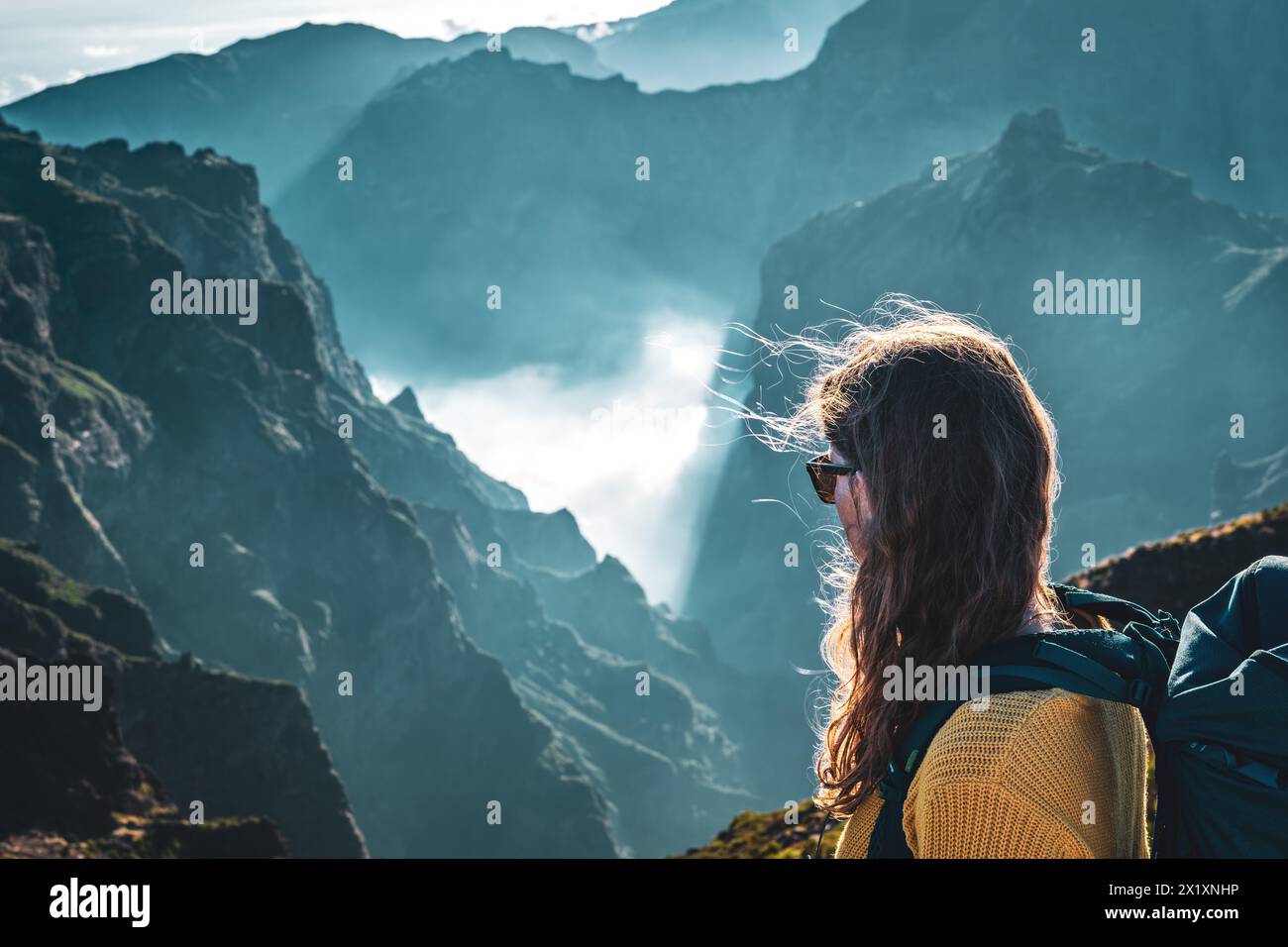 Description: Portrait of a female backpacker looking down into a deep, cloud-covered valley and enjoying the breathtaking view of the volcanic mountai Stock Photo