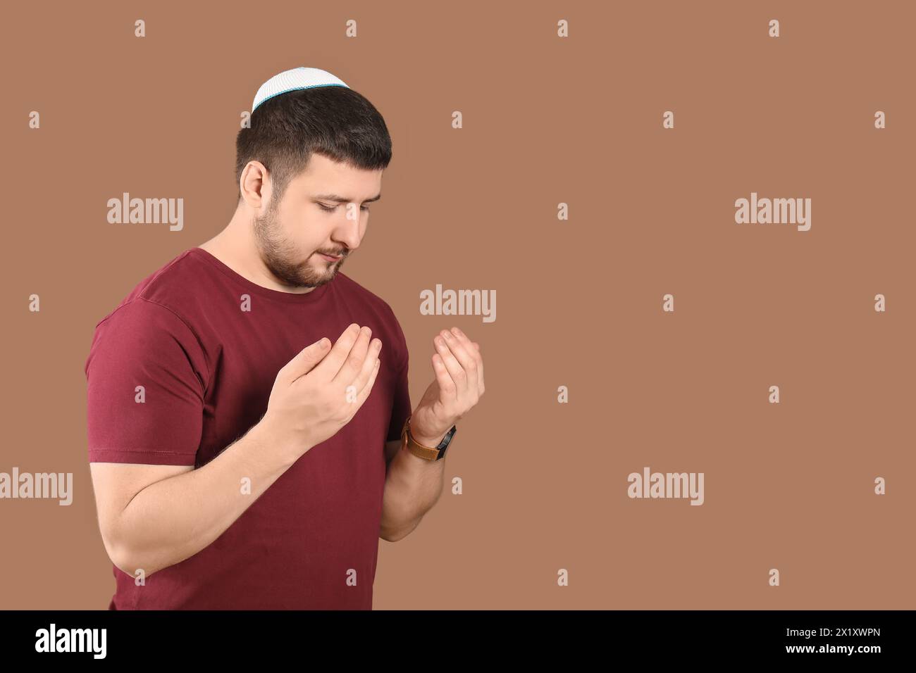 Young Jewish man in hat praying on brown background Stock Photo