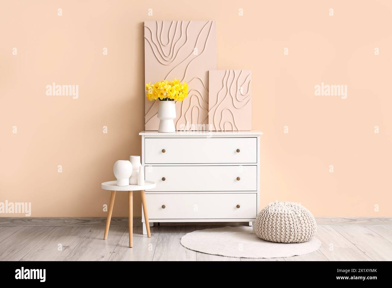 Chest of drawers with pictures and bouquet of narcissus flowers in beige room Stock Photo