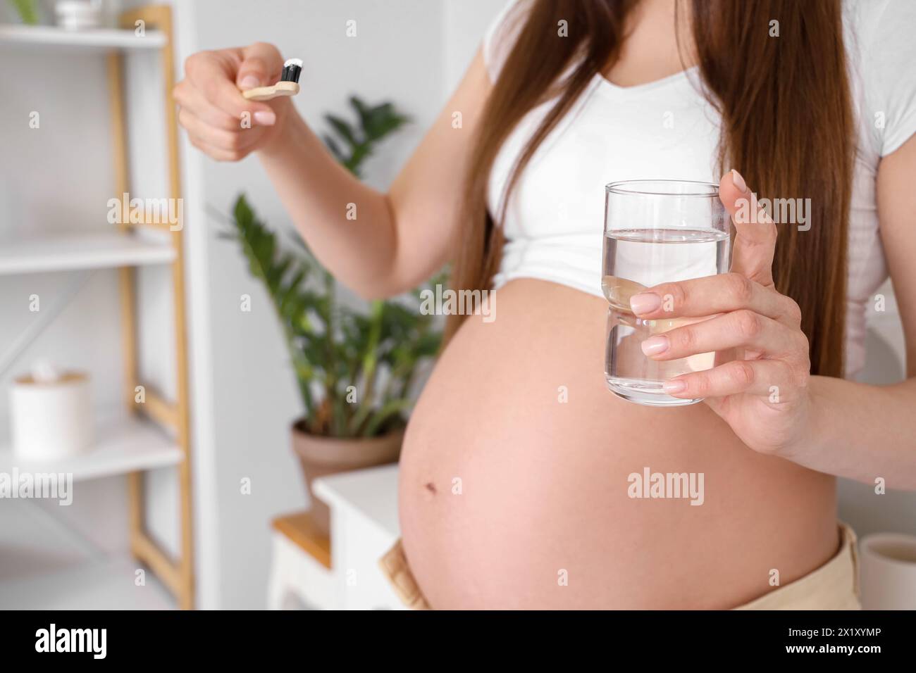 Young pregnant woman with tooth brush and glass of water in light bathroom, closeup Stock Photo