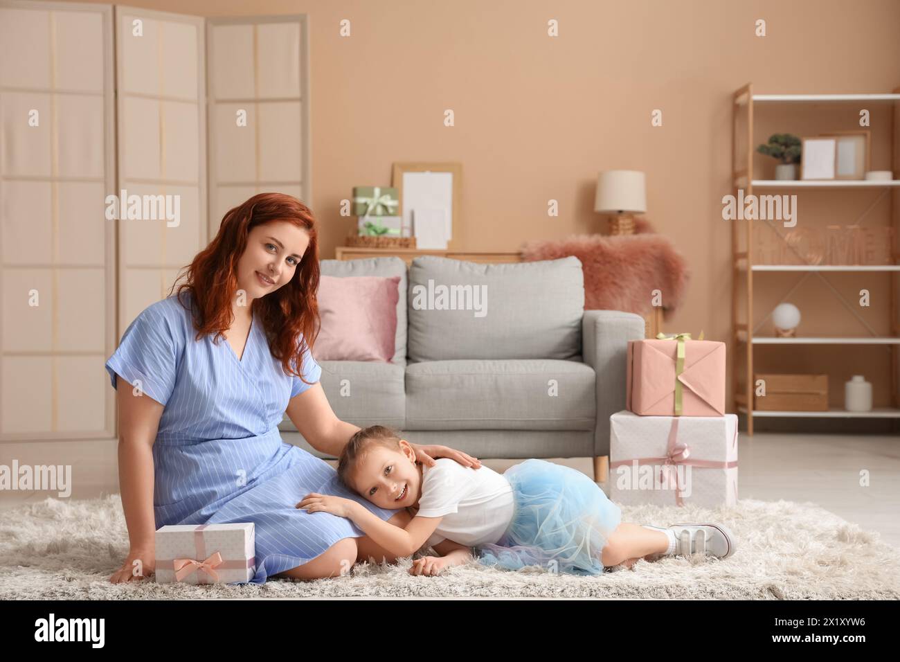 Little girl lying on her mother's  knees in living room. Mother's Day Stock Photo