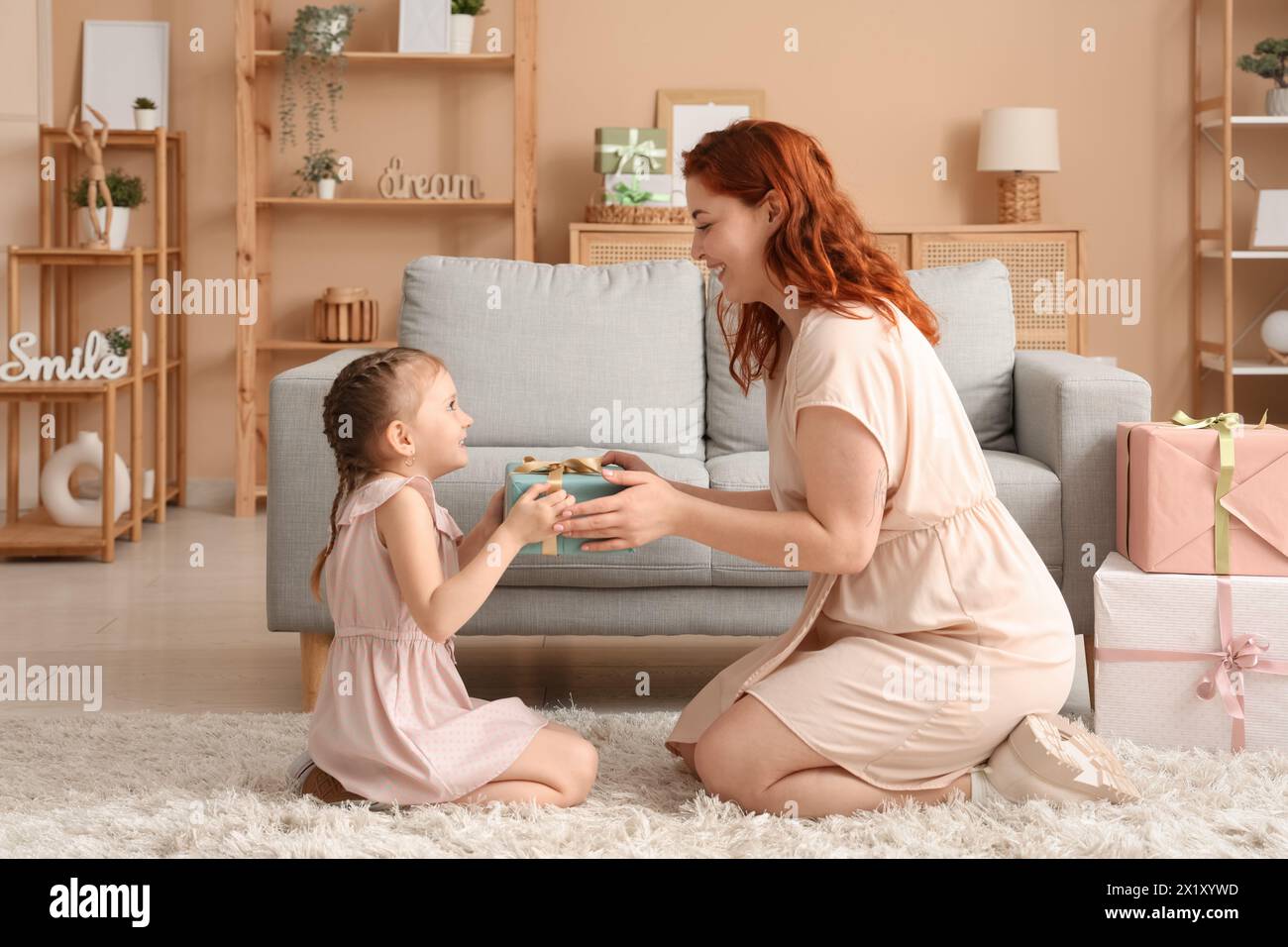 Little girl giving her mother gift for Mother's Day in living room Stock Photo