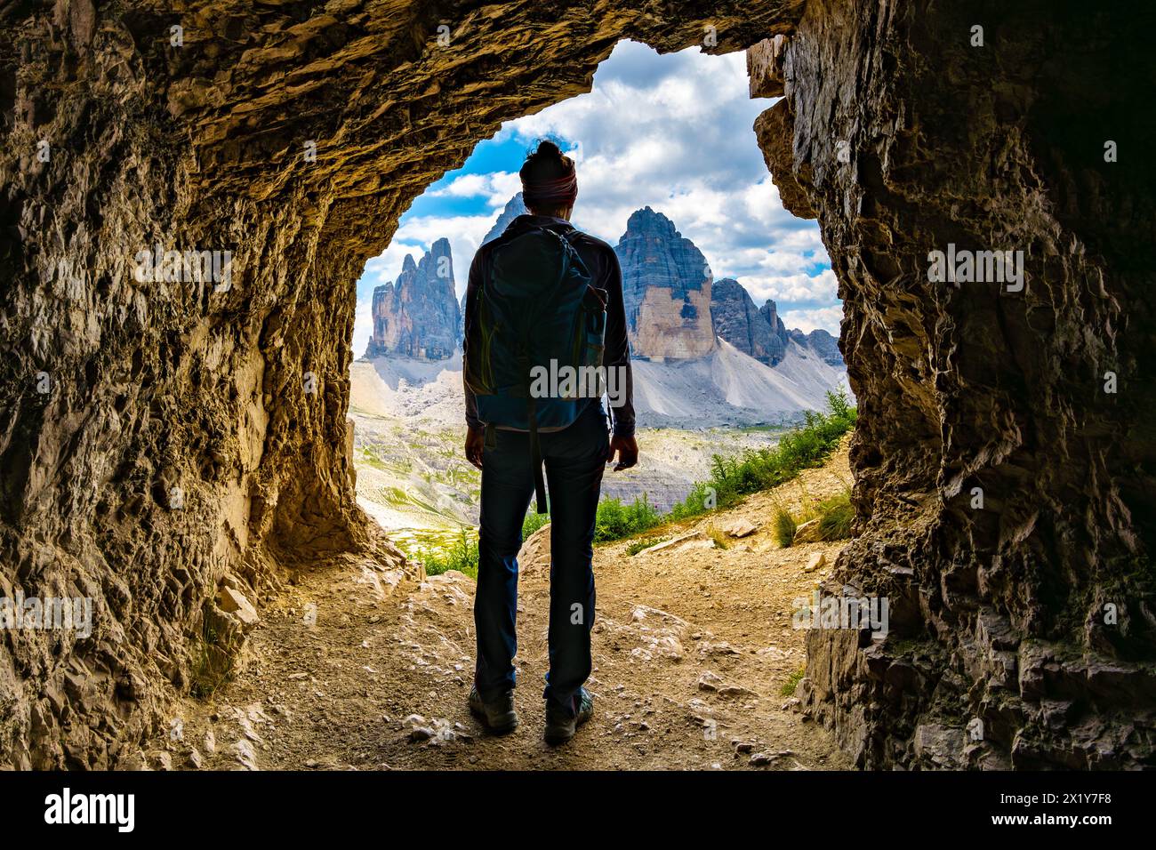 Description: Young athletic woman enjoys view on Tre Cime mountain range from a small cave in the morning. Tre Cime, Dolomites, South Tirol, Italy, Eu Stock Photo