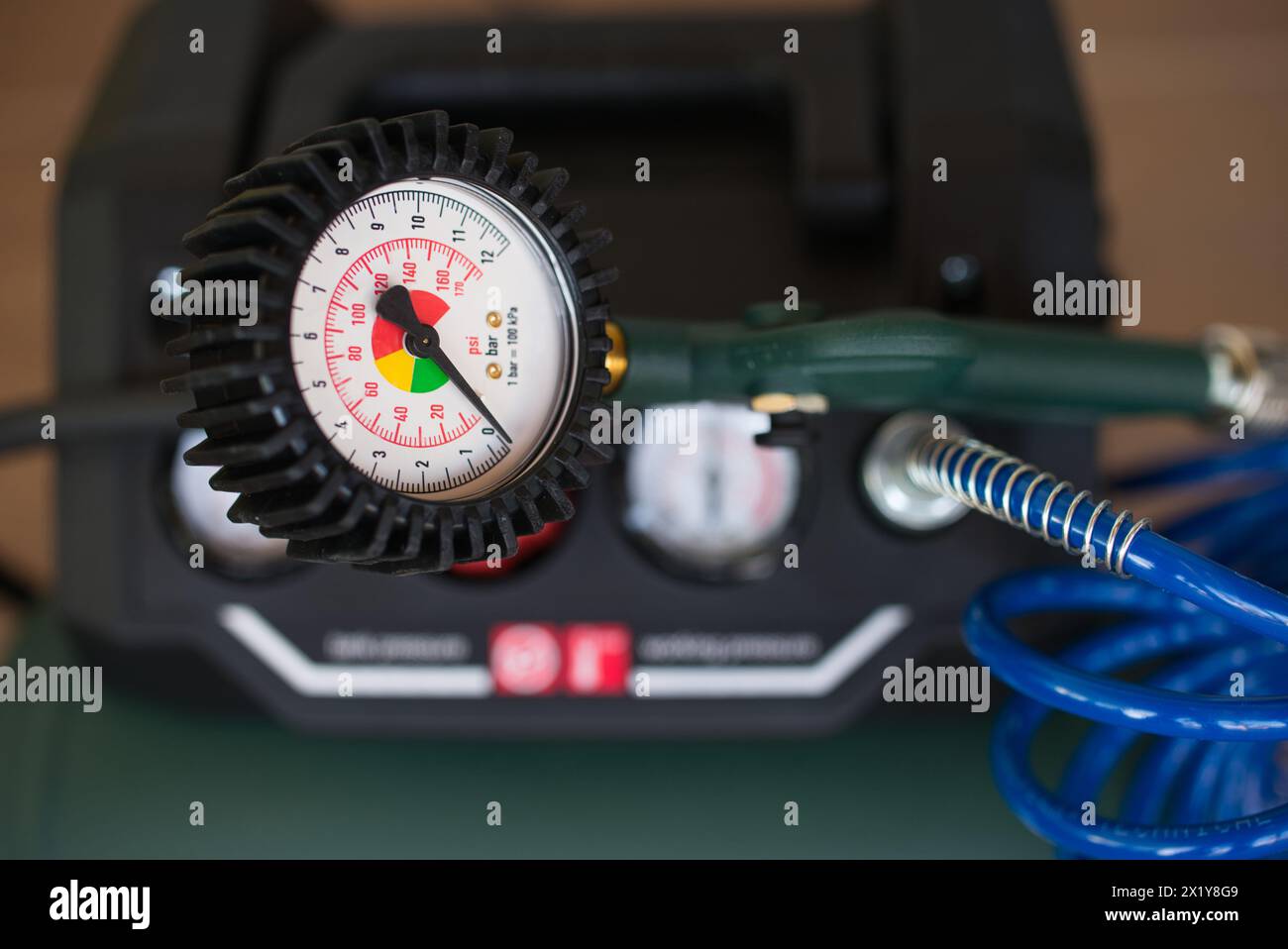 Analog air pressure gauge with a green compressor and blue spiral hose in the background. Stock Photo