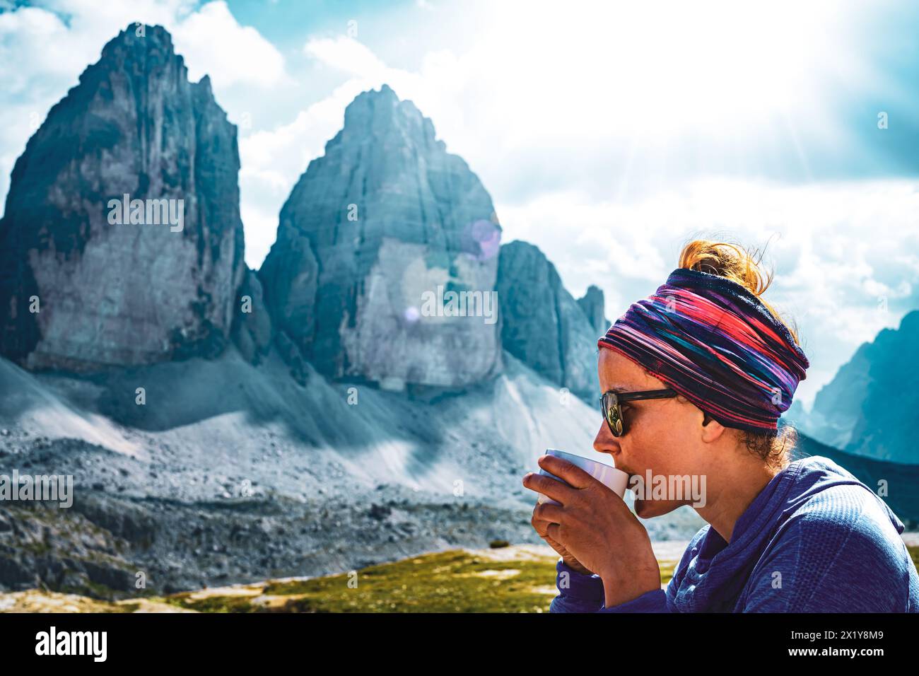 Description:  Young athletic woman enjoys coffee break with wonderful view on Tre Cime during sunny afternoon. Tre Cime, Dolomites, South Tirol, Italy Stock Photo