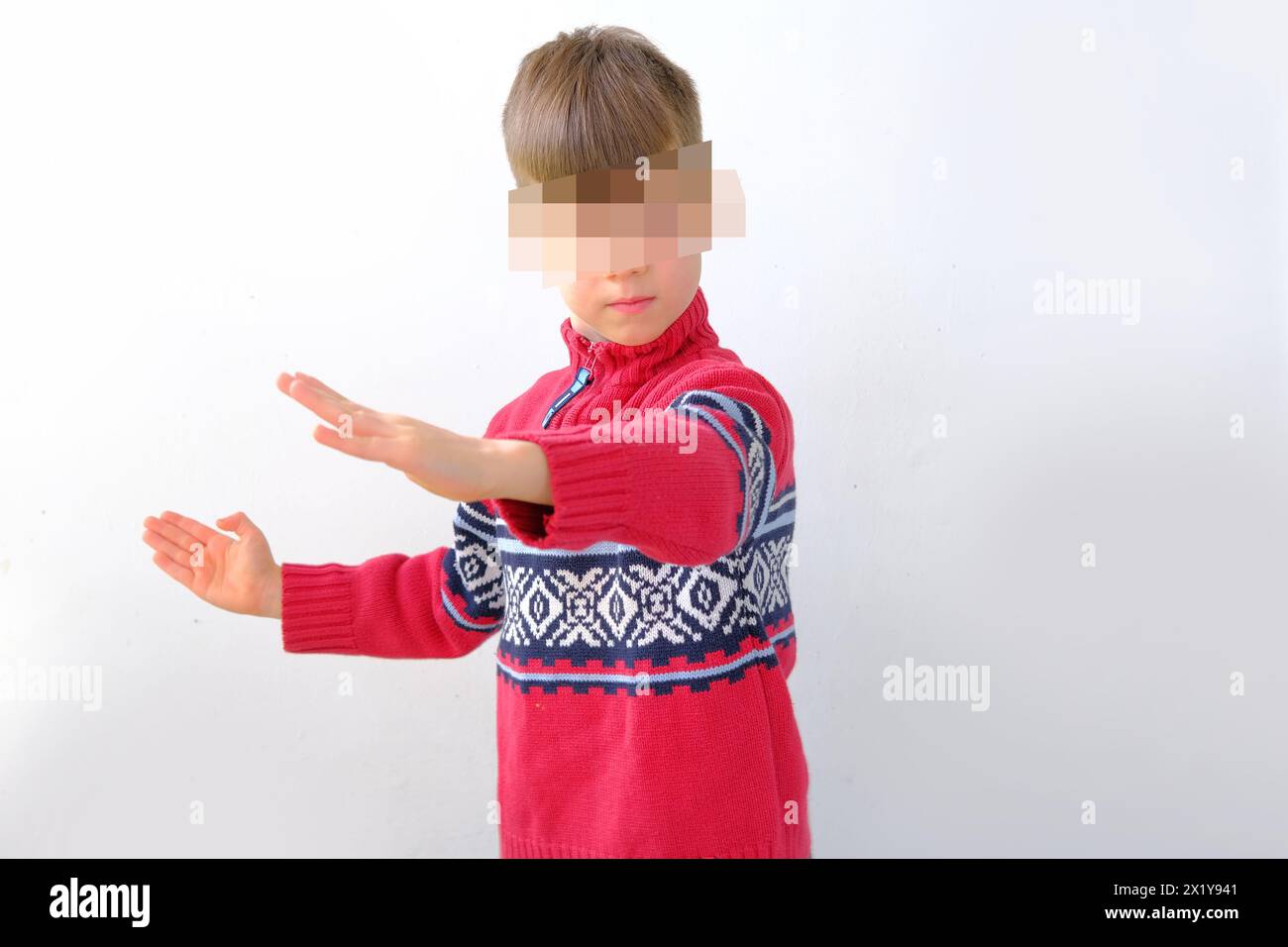 offended or punished child, a boy of 7-8 years old in a red Scandinavian sweater, kid's face is hidden by protective pixels, concept of personal data Stock Photo