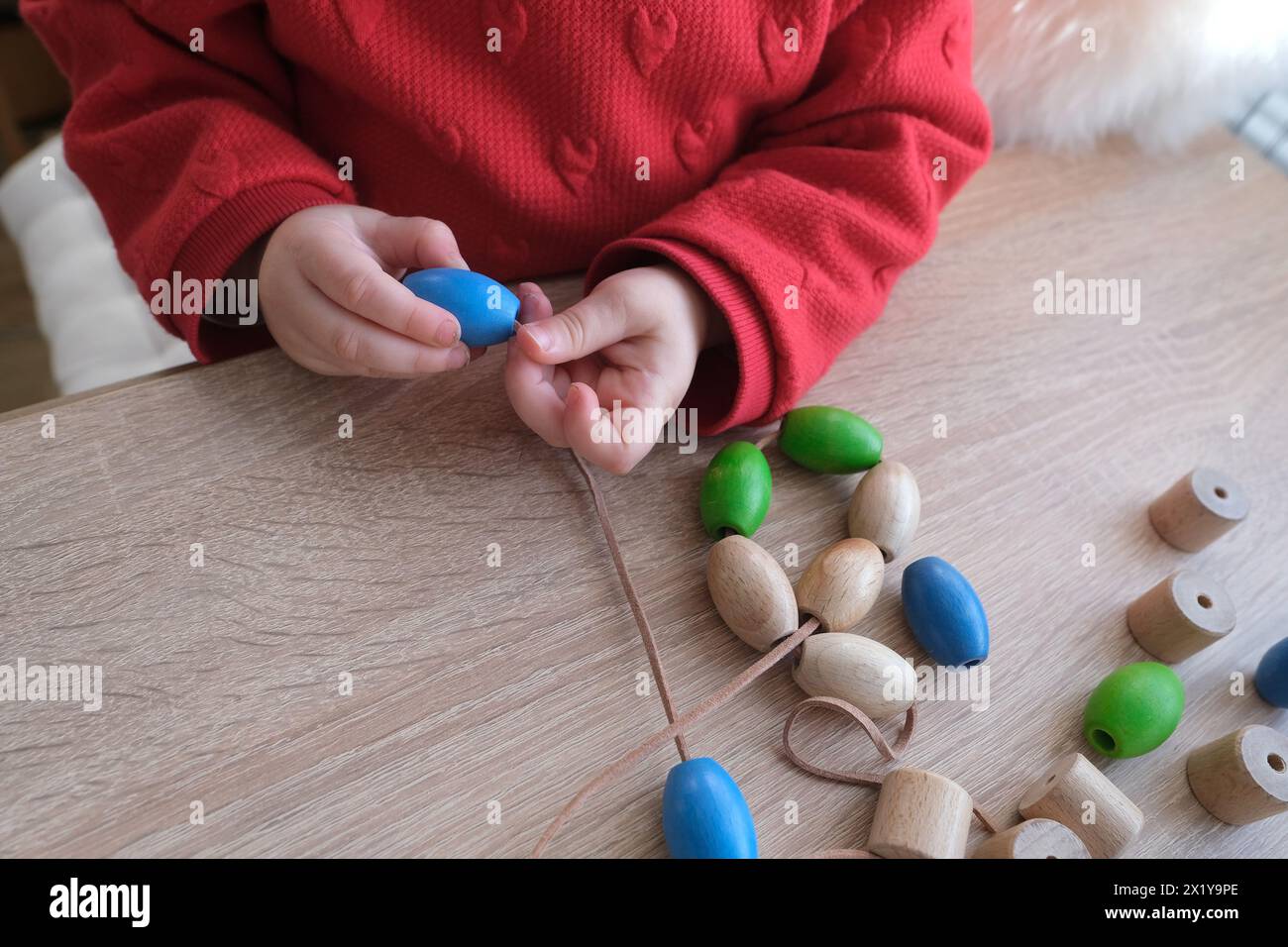 small child, toddler stringing colored wooden beads on a string ...