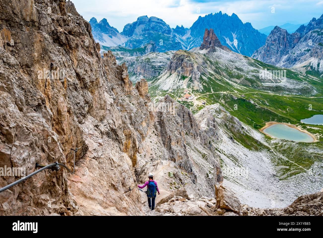 Description: Young athletic woman enjoys view on Drei-Zinnen-Hütte from via ferrata in the evening. Tre Cime, Dolomites, South Tirol, Italy, Europe. Stock Photo