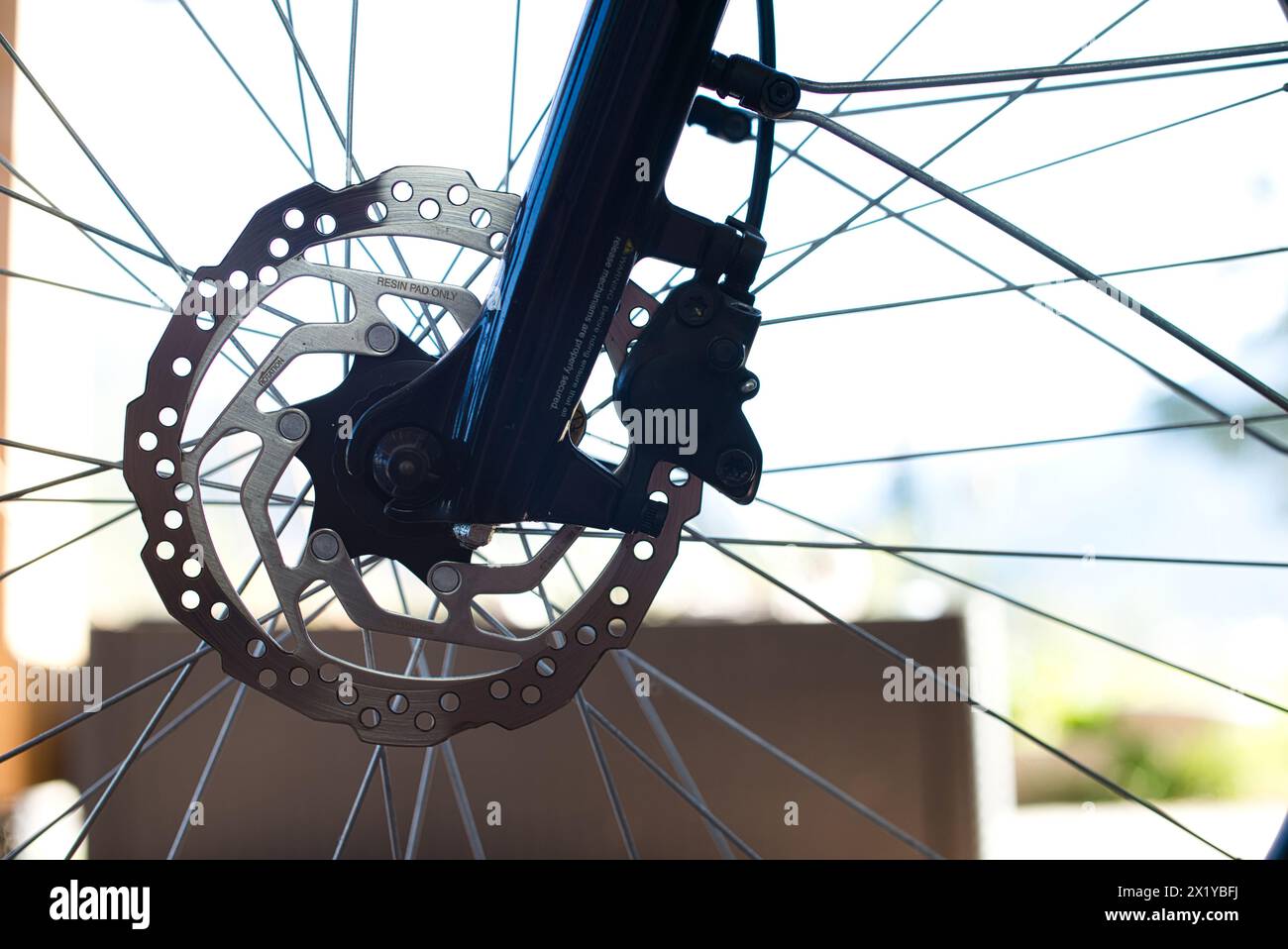 Close-up view of the front wheel of an E-bike, showcasing a stainless steel brake disc, brake caliper, and a section of the dark blue glossy fork. Stock Photo