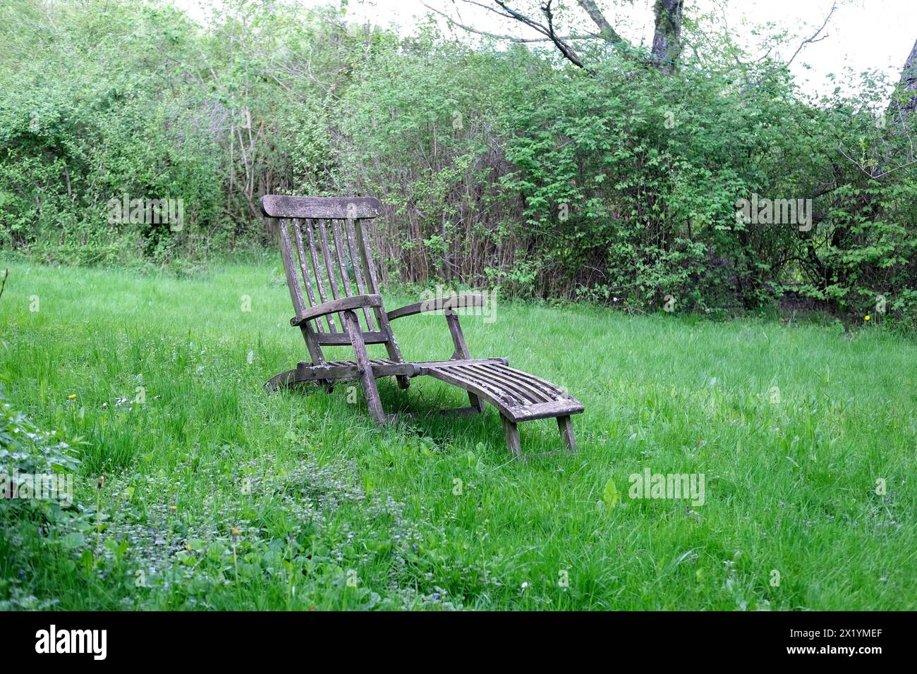 old wooden armchair, chaise longue stands on a green lawn in a spring garden, trees in the background, relaxation concept, enjoyment in life, idyll Stock Photo