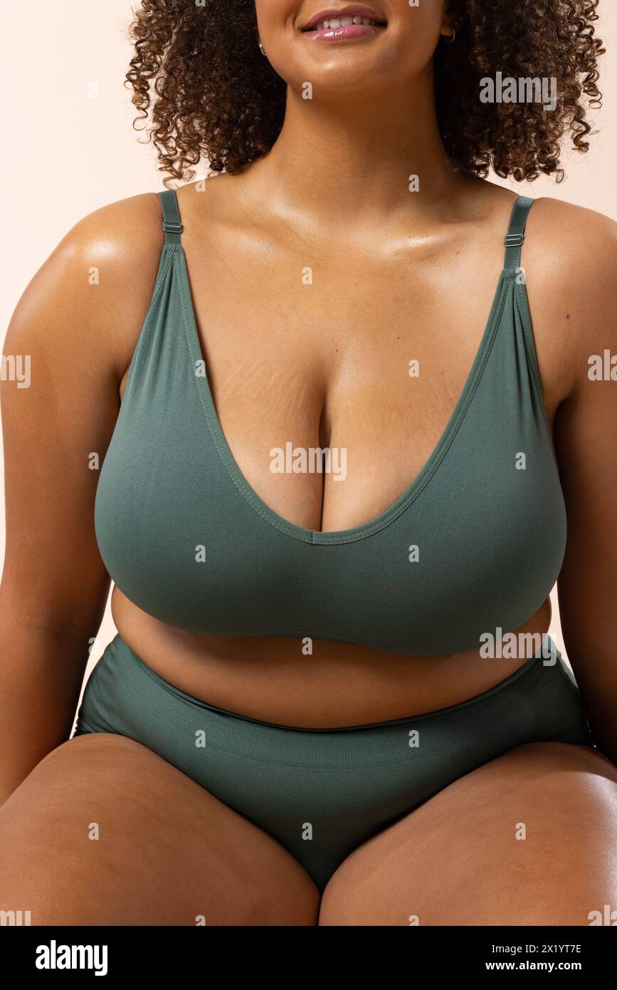 Biracial young female plus size model with curly hair in a green swimsuit on a beige background Stock Photo