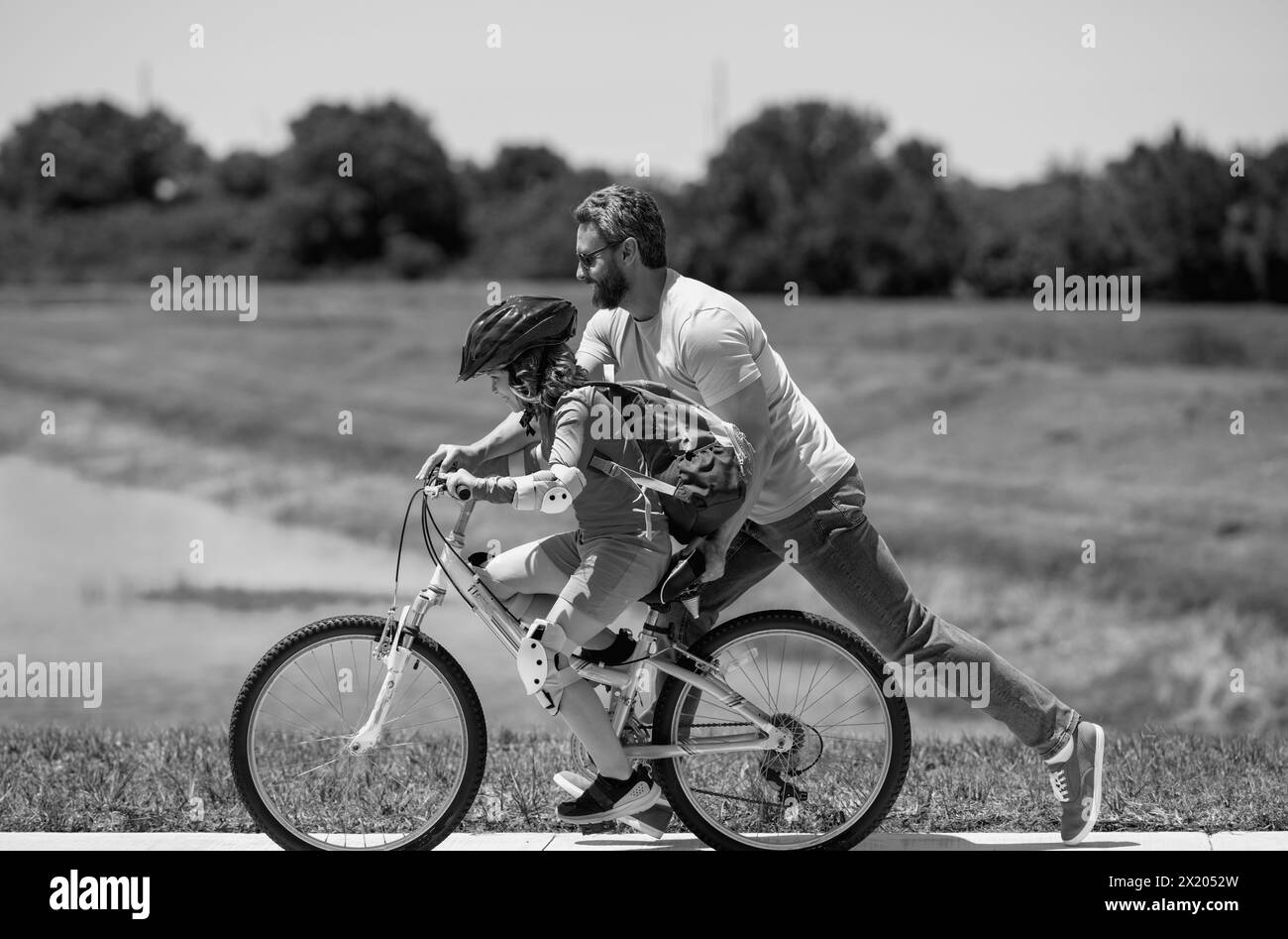 Happy Fathers day. Father and son in bike helmet for learning to ride bicycle at park. Father helping son cycling. Father and son on the bicycle on Stock Photo