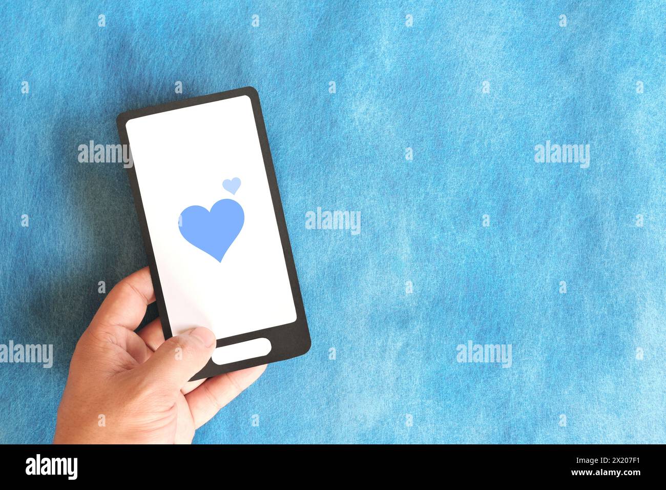 Human hand holding mobile phone with blue heart icon. Kindness, love ...