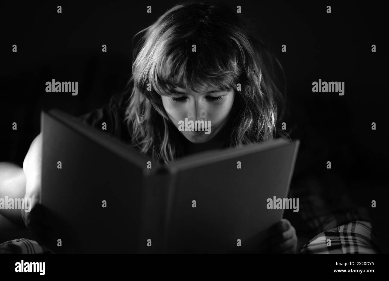 Child little boy reading a book in the dark home. Kids face with night