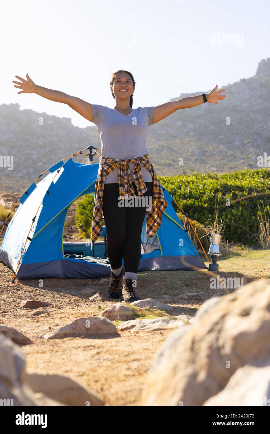 Biracial female hiker with open arms enjoying nature near tent Stock Photo