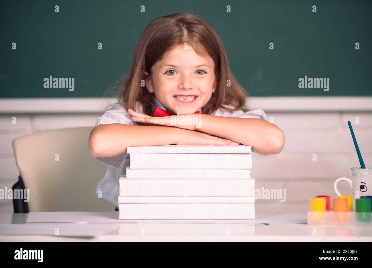 Smiling girl sitting at the desk and holding hands on the books in the ...