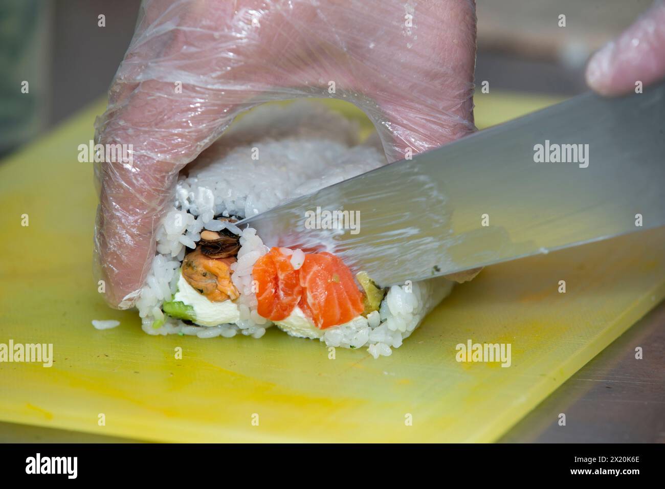 A gloved hand cuts sushi on a cutting board. Stock Photo
