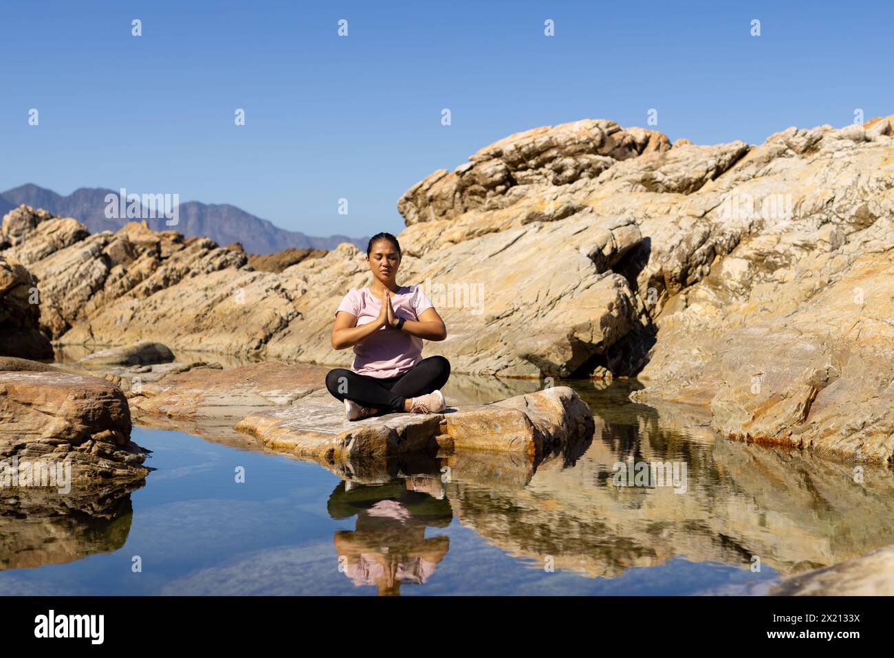Biracial female hiker meditating by mountain water, copy space Stock Photo