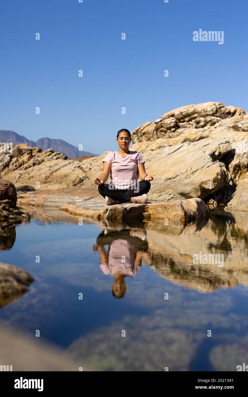 Biracial female hiker meditating by mountain water, copy space Stock Photo