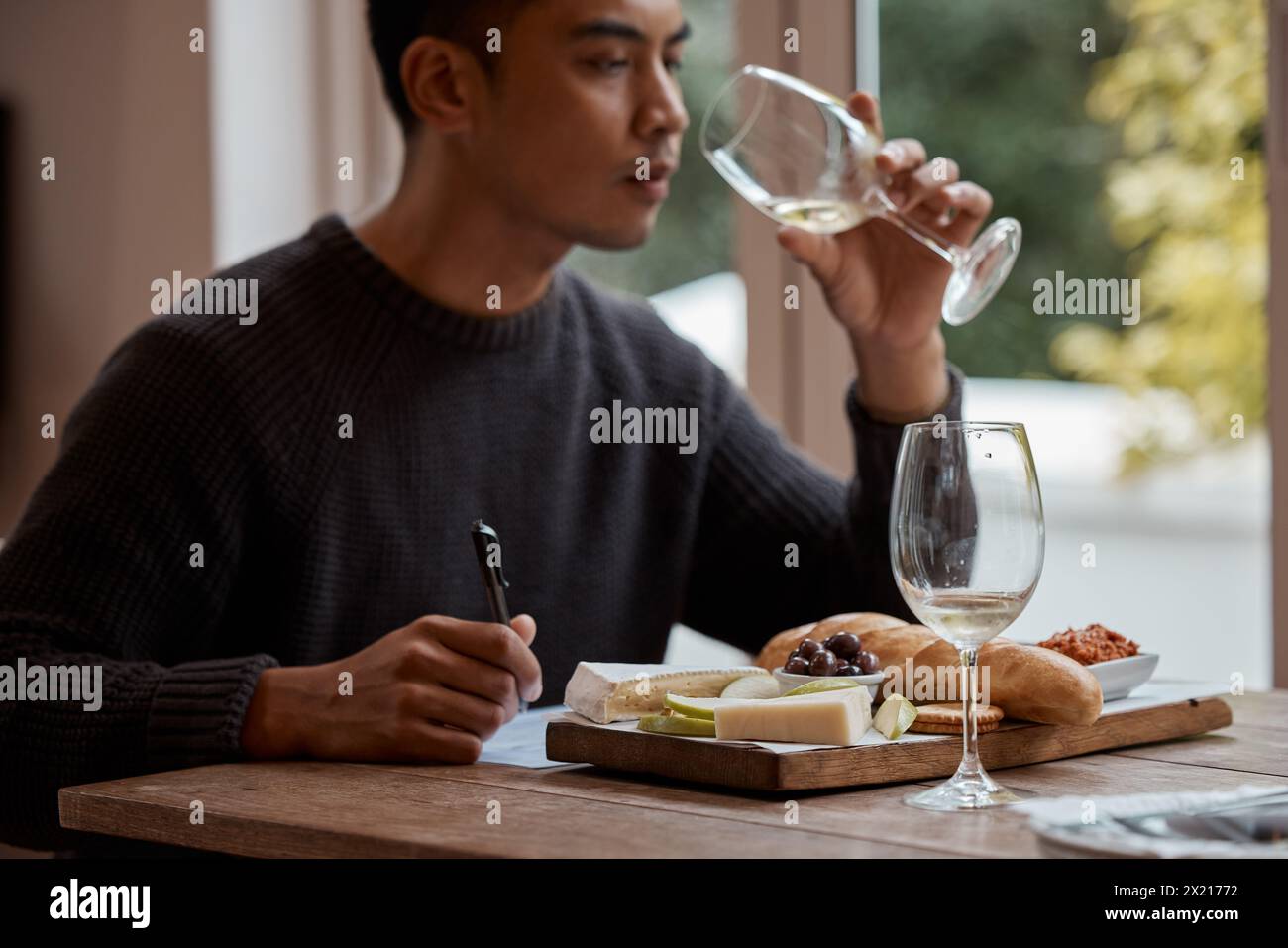 Drinking, eating and restaurant with asian man food critic writing notes for review as customer. Cheese platter, glass and wine with consumer person Stock Photo