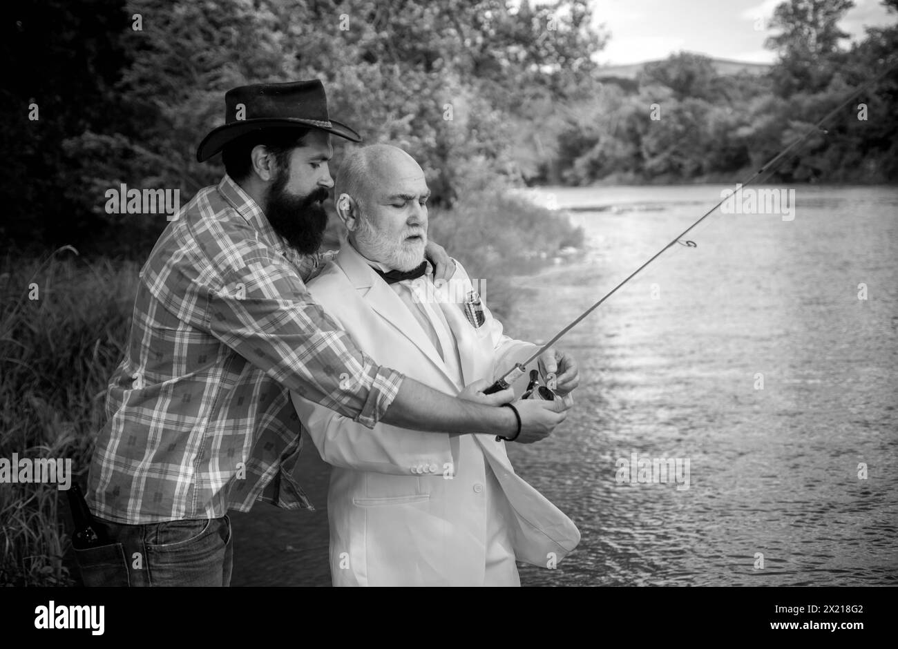 Two men friends fishing. Flyfishing angler makes cast, standing in river water. Old and young fisherman. Stock Photo