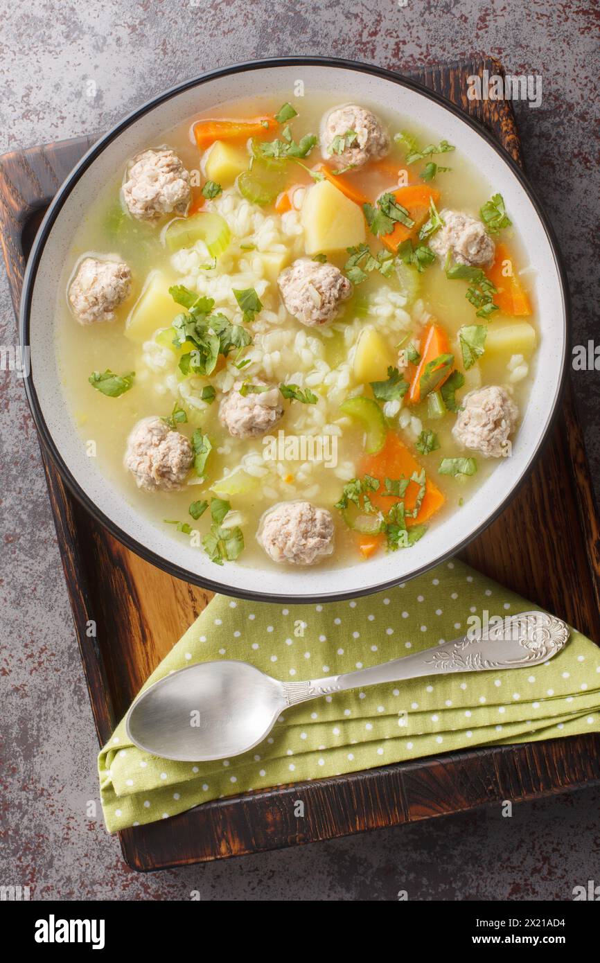 Rice soup with meatballs and vegetables close-up in a bowl on the table. Vertical top view from above Stock Photo
