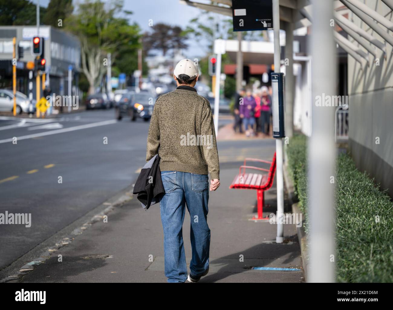 Man walking to the bus stop on a busy suburban street. Unrecognizable people walking on the pedestrian sidewalk. Auckland. Stock Photo