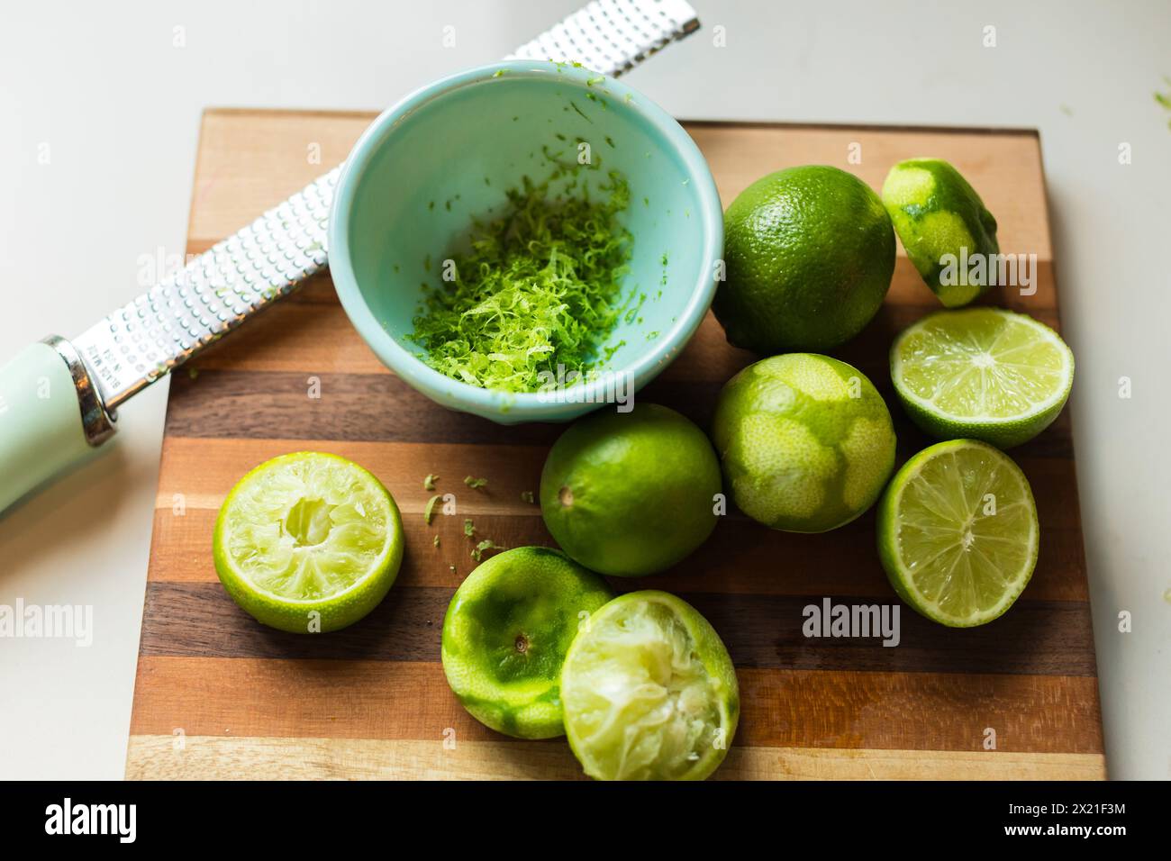 Zested and halved limes on a striped cutting board Stock Photo