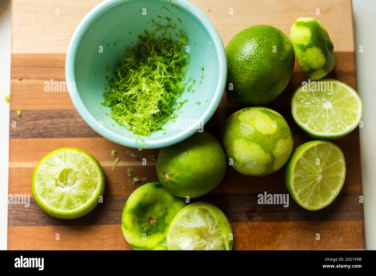 Zested and halved limes on a striped cutting board Stock Photo