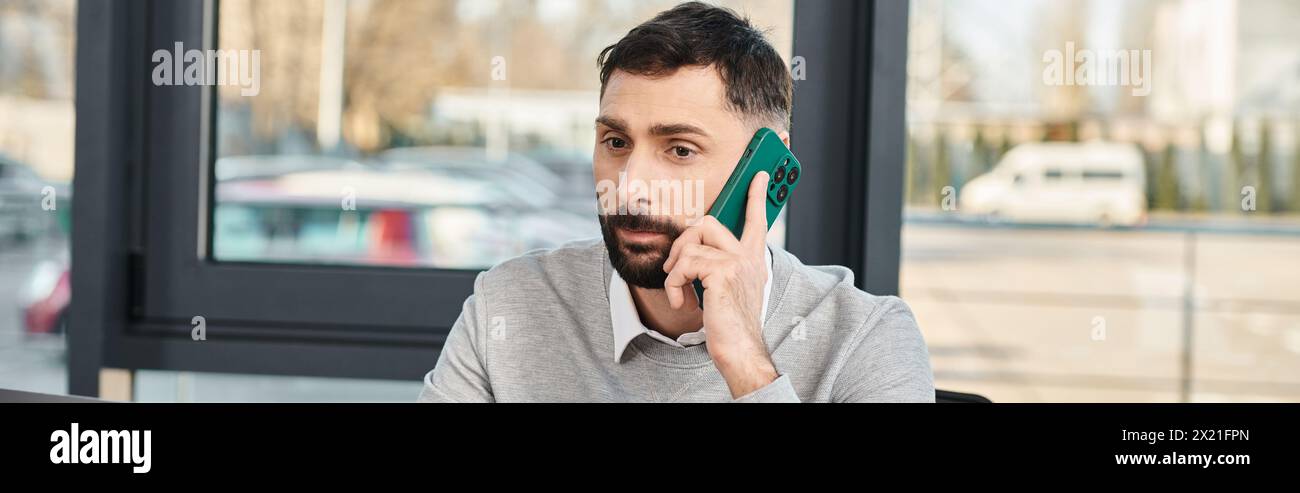 A man in business attire sits at a table in an office, focused on a cell phone conversation. Stock Photo