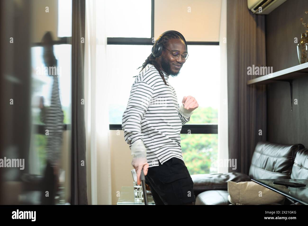 Carefree happy young African man listening to music in headphones, enjoying housework Stock Photo
