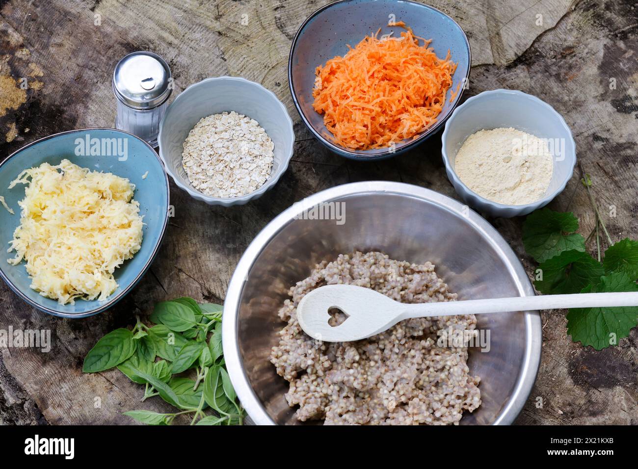 Making vegan herb patties, step 1: Ingredients; cooked buckwheat, fresh wild herbs, grated potatoes, grated carrots, chickpea flour, fine rolled oats, Stock Photo