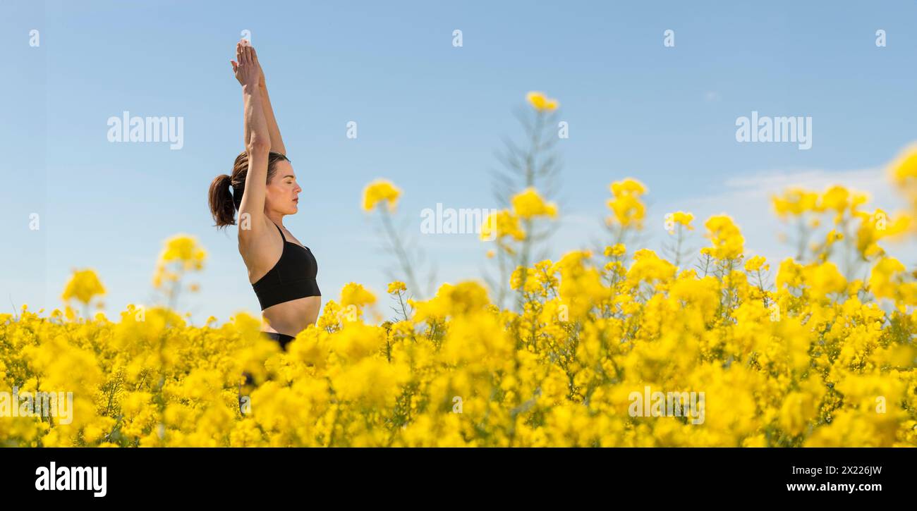 A woman meditating and enjoying the outdoors in a yellow canola flower field Stock Photo