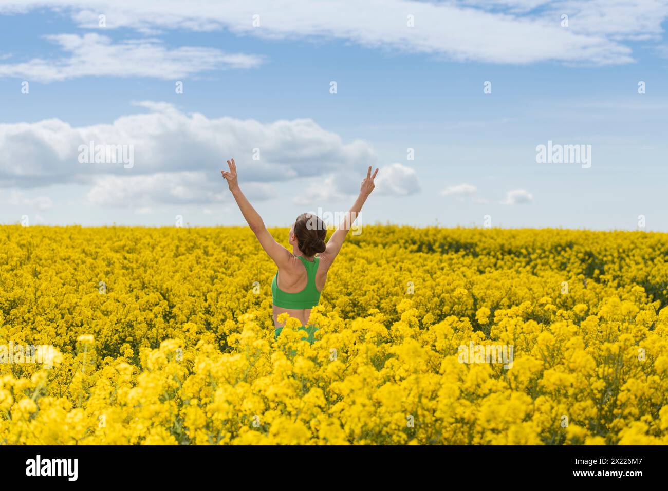 Sporty woman with arms raised in celebration and enjoying the sun in a yellow rapeseed field Stock Photo