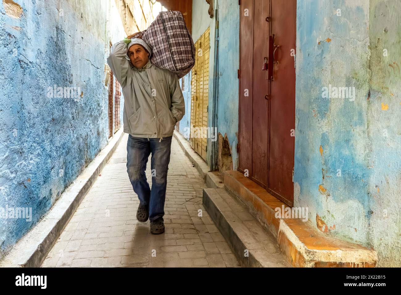 A porter man is walking down a tight alleyway in the medina of Fez, Morocco. Stock Photo