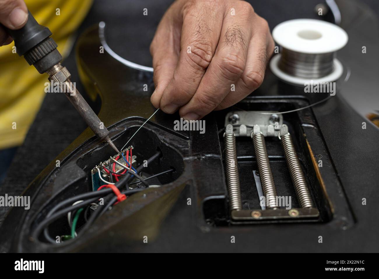 Latin American luthier's hands soldering with a soldering iron and tin