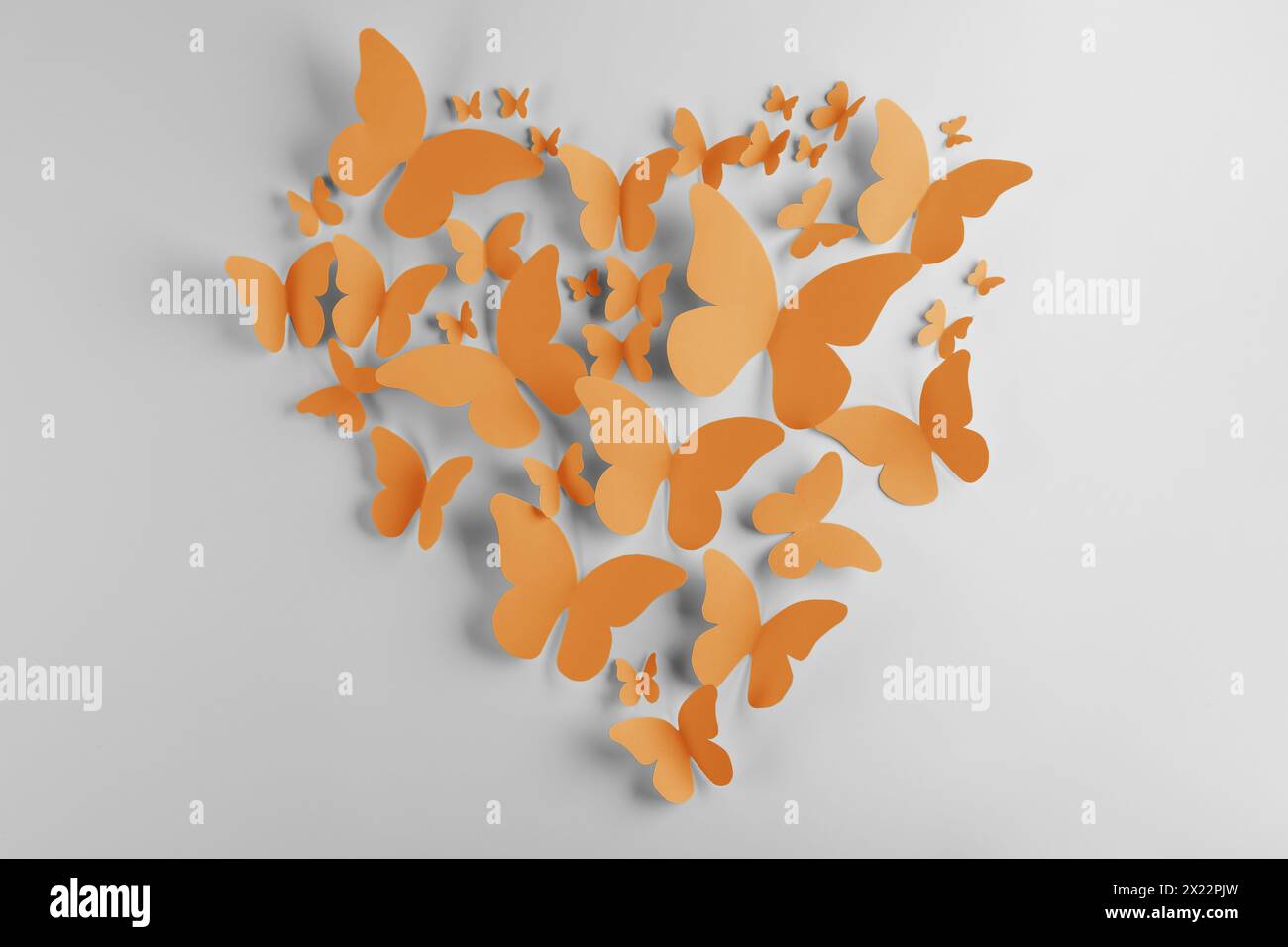 Heart made of orange paper butterflies on white wall Stock Photo