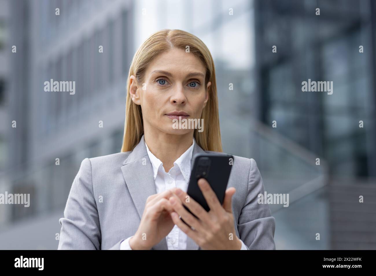 A confident businesswoman in a grey suit uses her smartphone against a