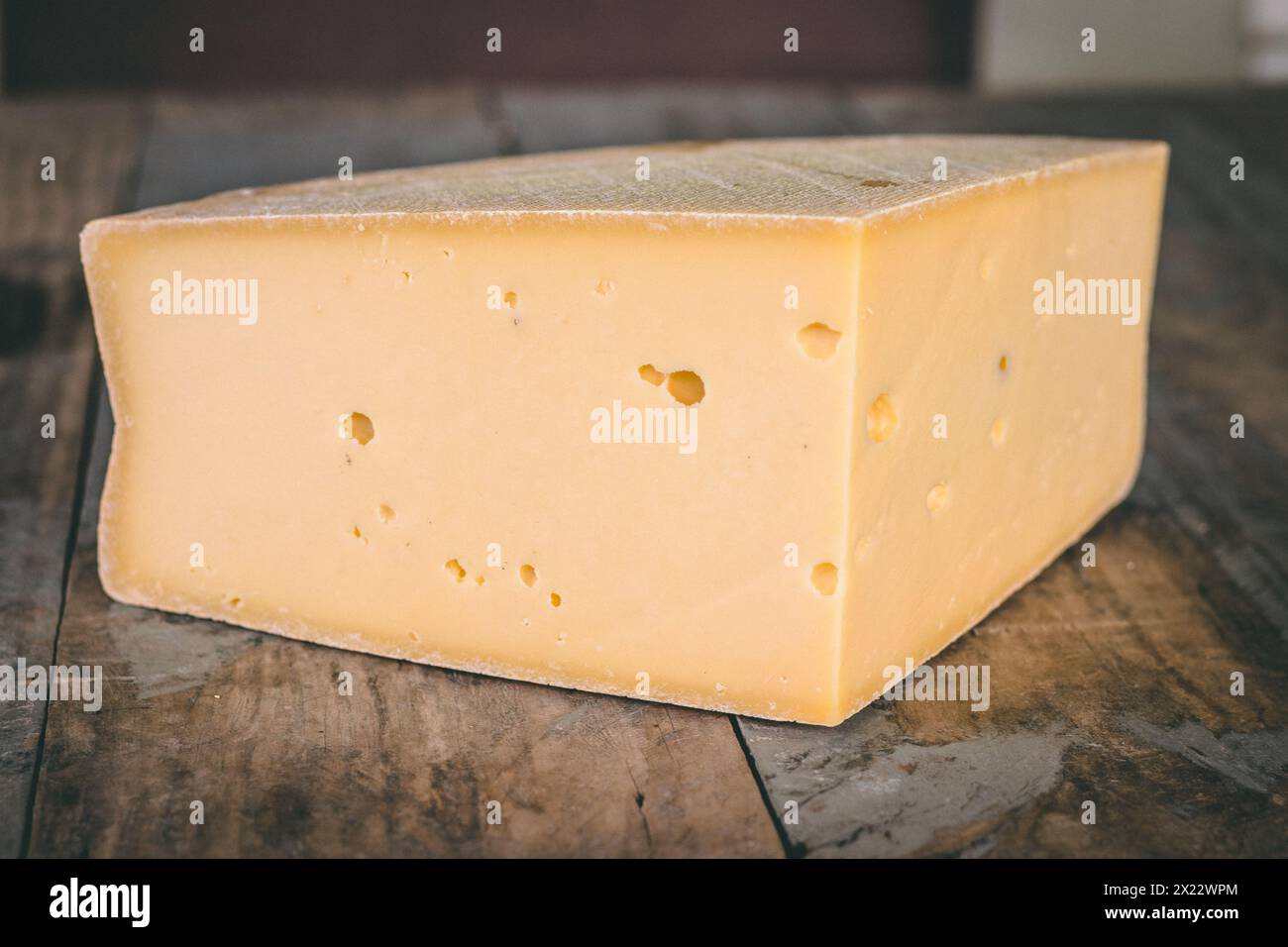 Close-up block of alpine hard cheese with rind and eyes on rustic wood table Stock Photo