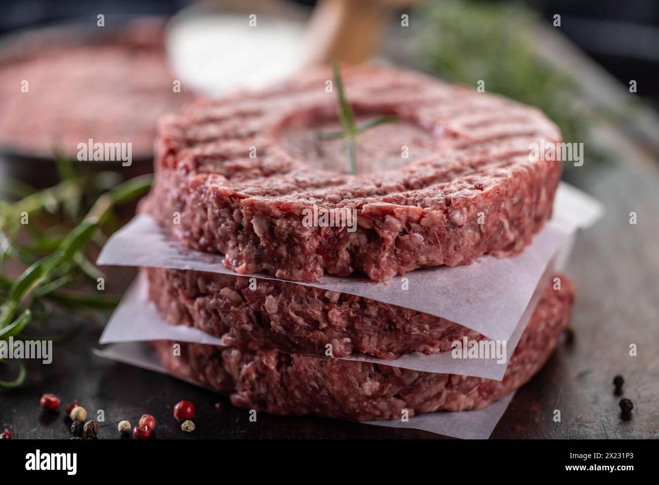 Fresh raw ground beef patties with rosemary salt and pepper made in a meat form on a cutting board. Stock Photo