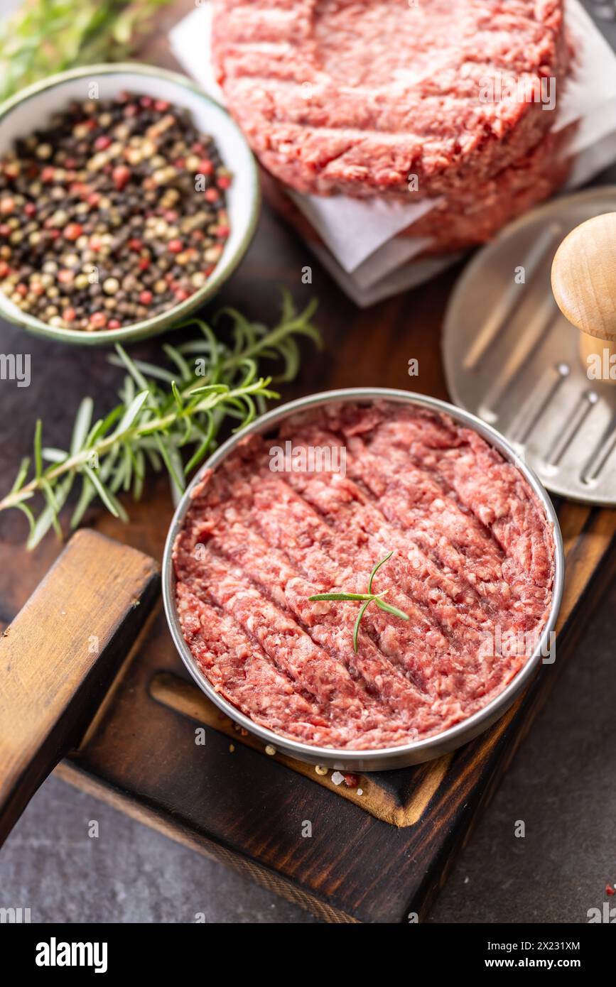 Fresh raw ground beef patties with rosemary salt and pepper made in a meat form on a cutting board. Stock Photo