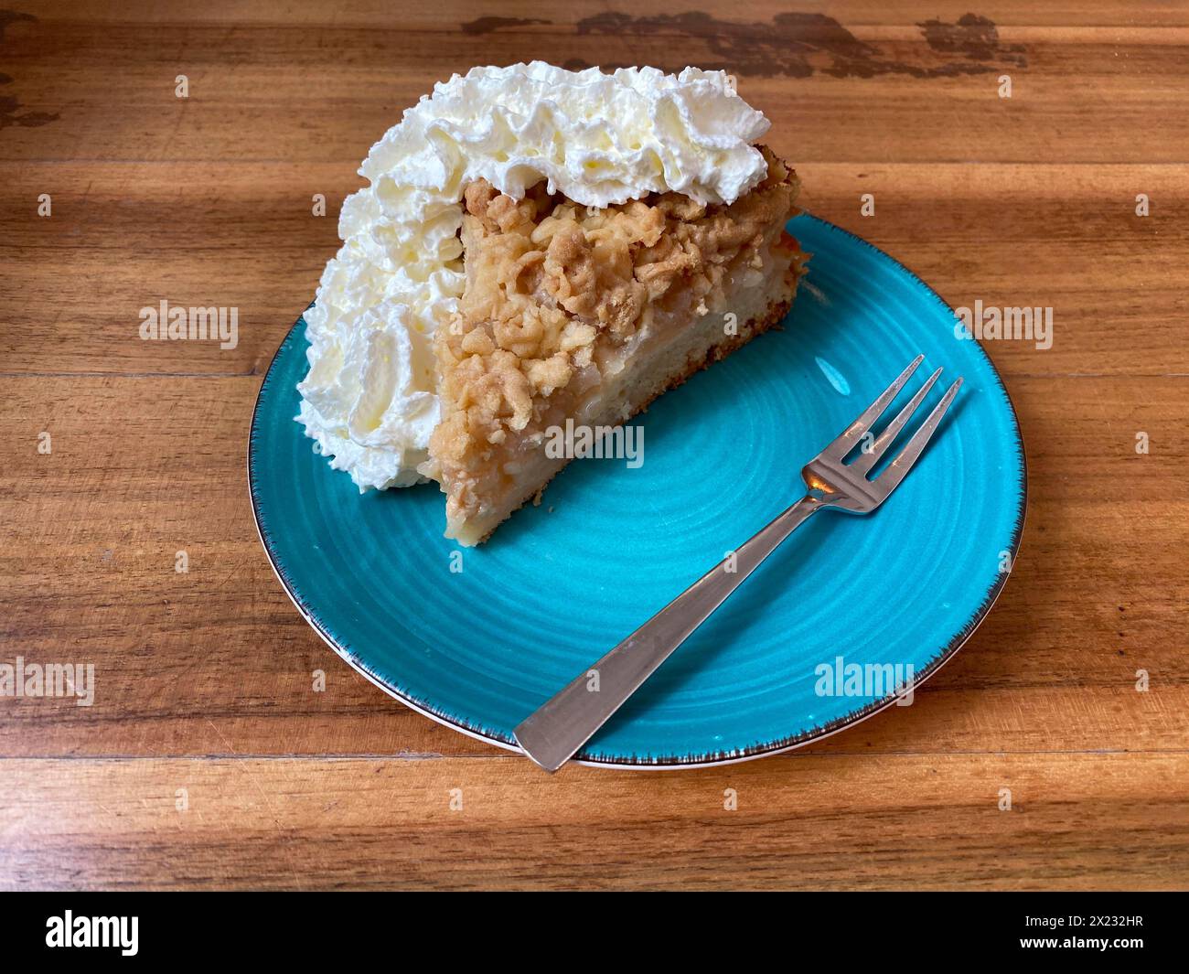 Piece of apple pie with whipped cream on plate, cake fork, wooden table, Frankfurt am Main