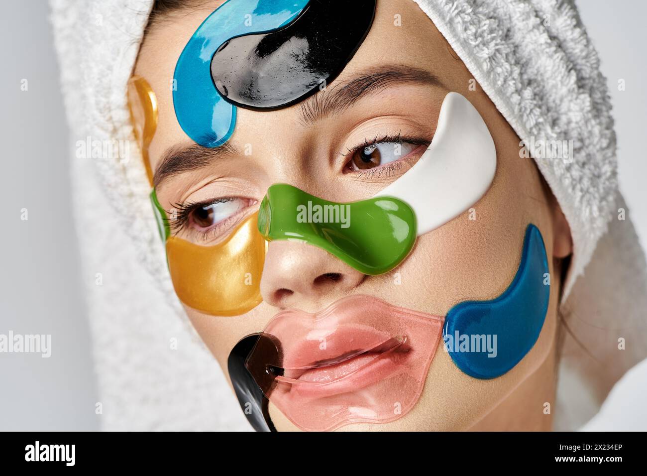 A young woman with eye patches on her face, towel wrapped on her head, exuding beauty and artistry. Stock Photo