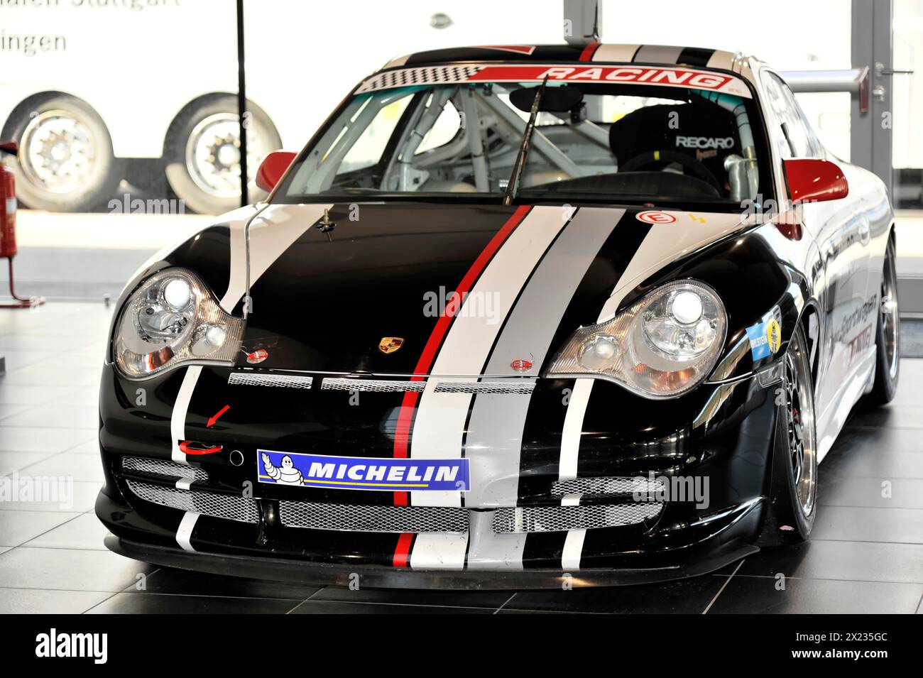A black Porsche racing car with white and red stripes stands in the