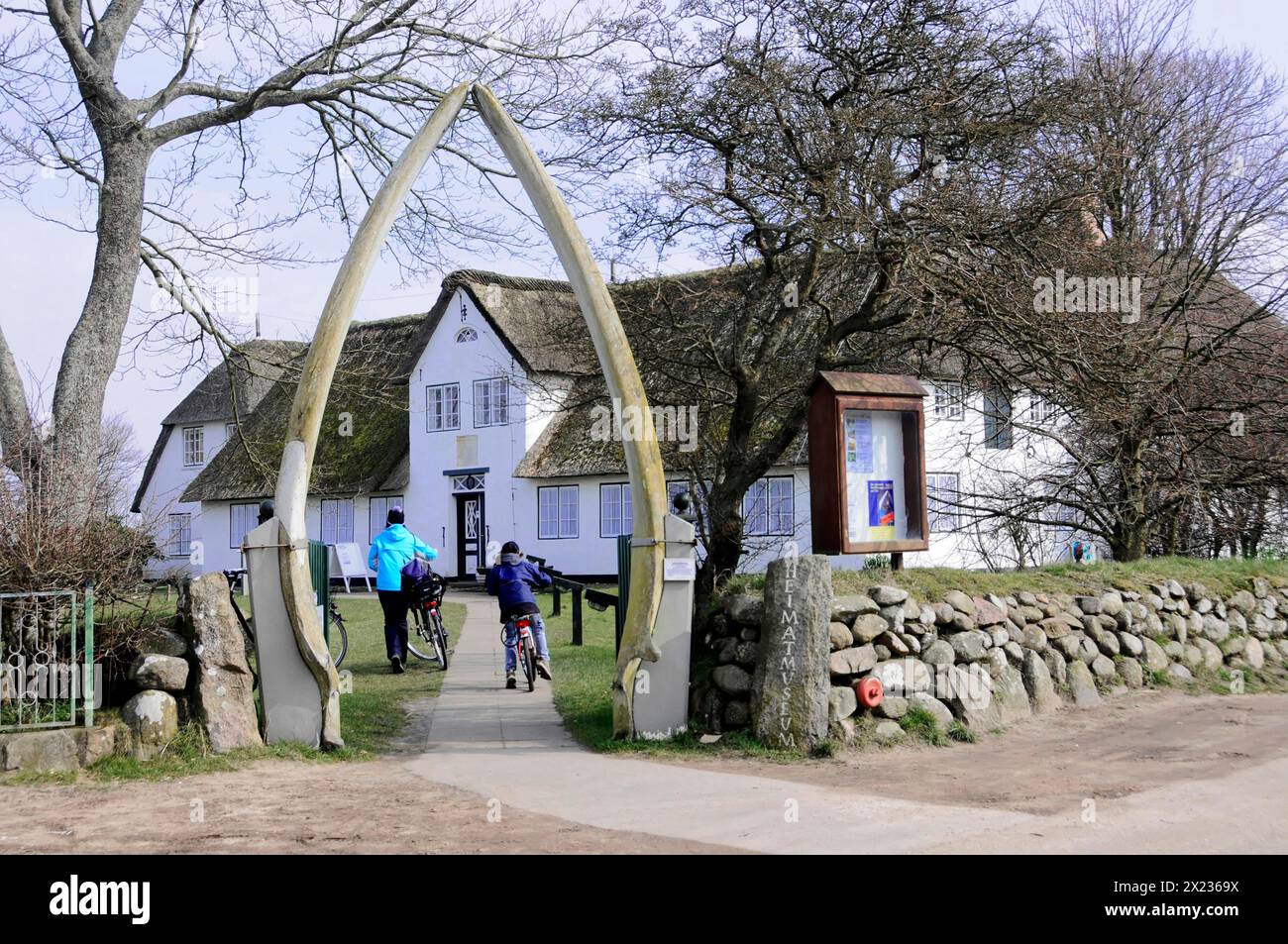 Sylt, North Frisian Island, Schleswig Holstein, Cyclists ride through an archway on a pebble path past historic houses, Sylt, North Frisian Island Stock Photo