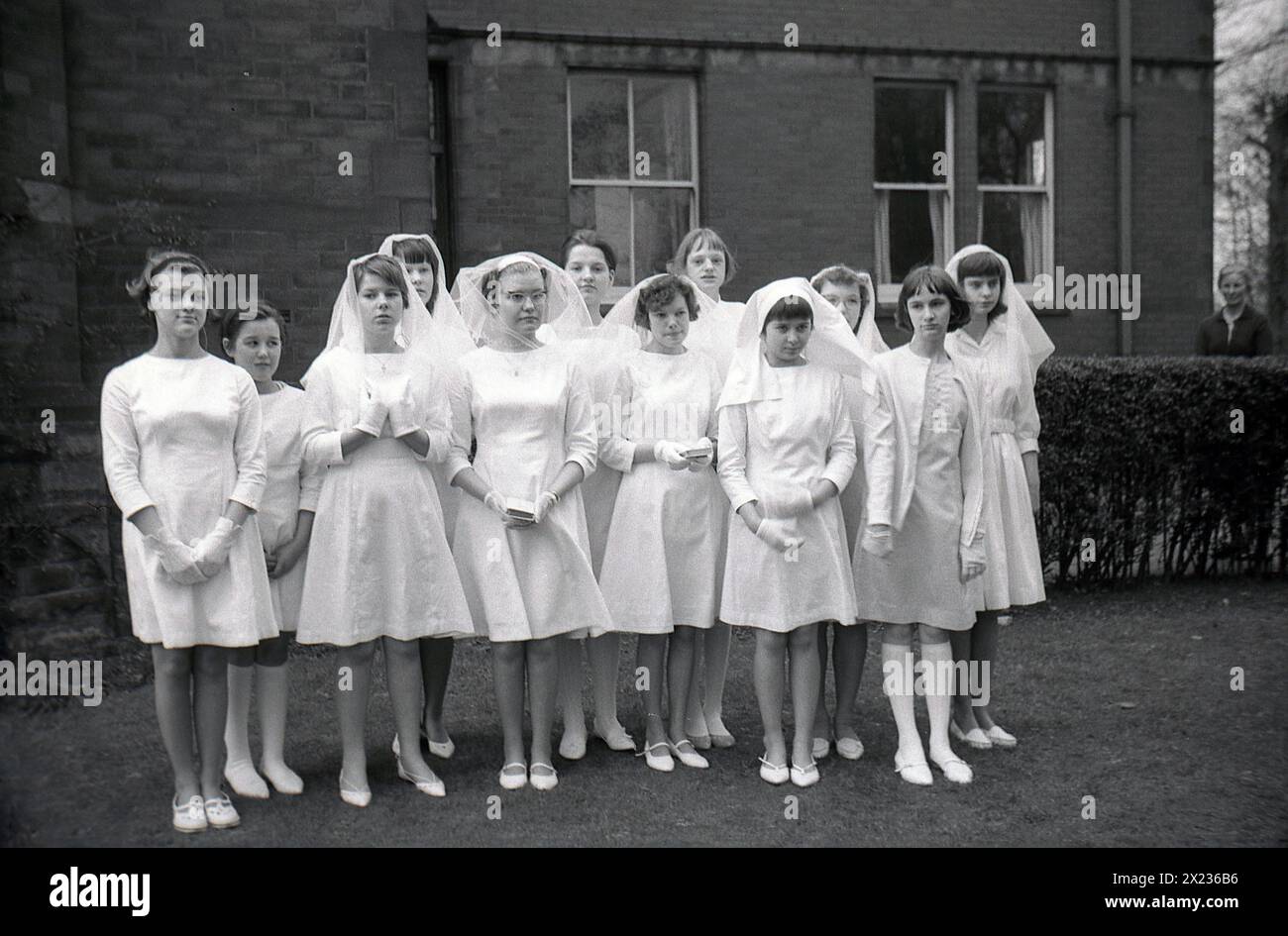 1970s, historical, catholic schoolgirls wearing white dresses and hair veils, standing for a photo after having their first holy communion, England, UK. Stock Photo