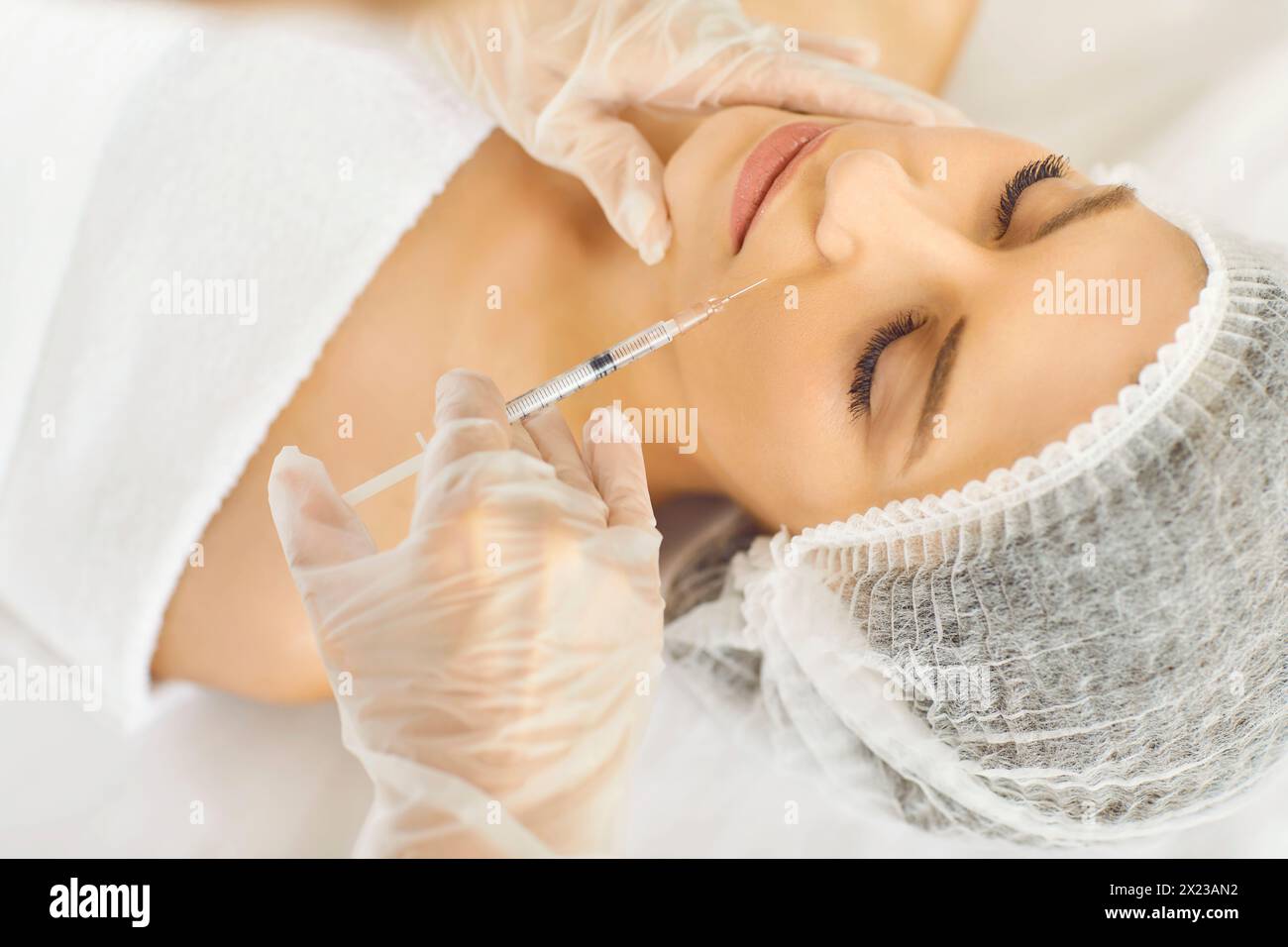 Young woman receives aesthetic injection treatment done by professional cosmetologist Stock Photo