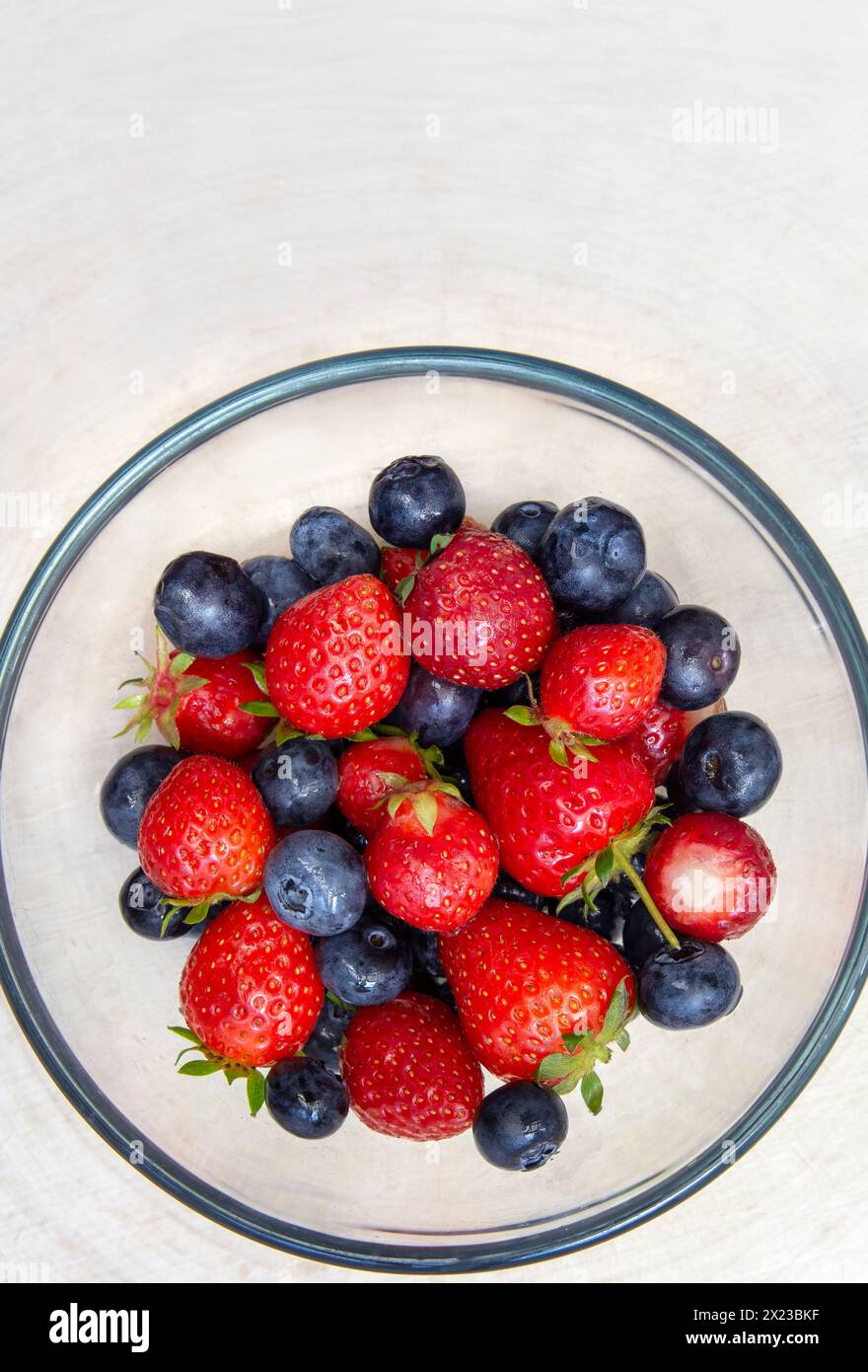 Overhead image of washed strawberries and blueberries in glass bowl on ...