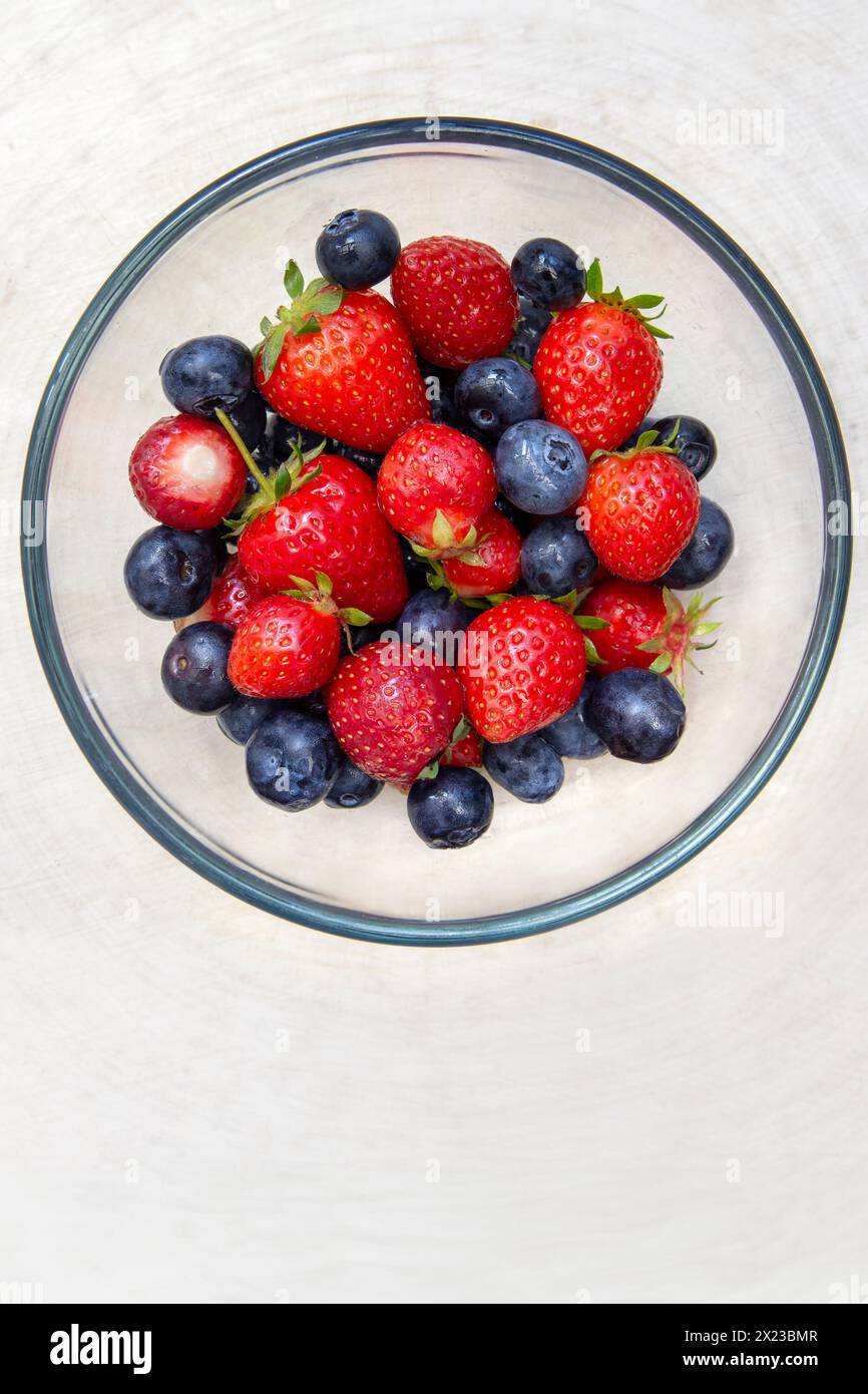 Overhead image of washed strawberries and blueberries in glass bowl on wooden table top Stock Photo